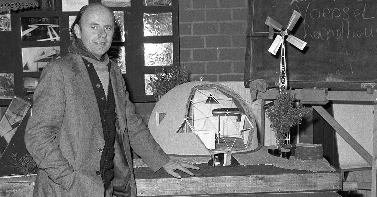 Zwart-wit foto van een man voor een maquette van De Kleine Aarde met een ronde koepel en een windmolen.