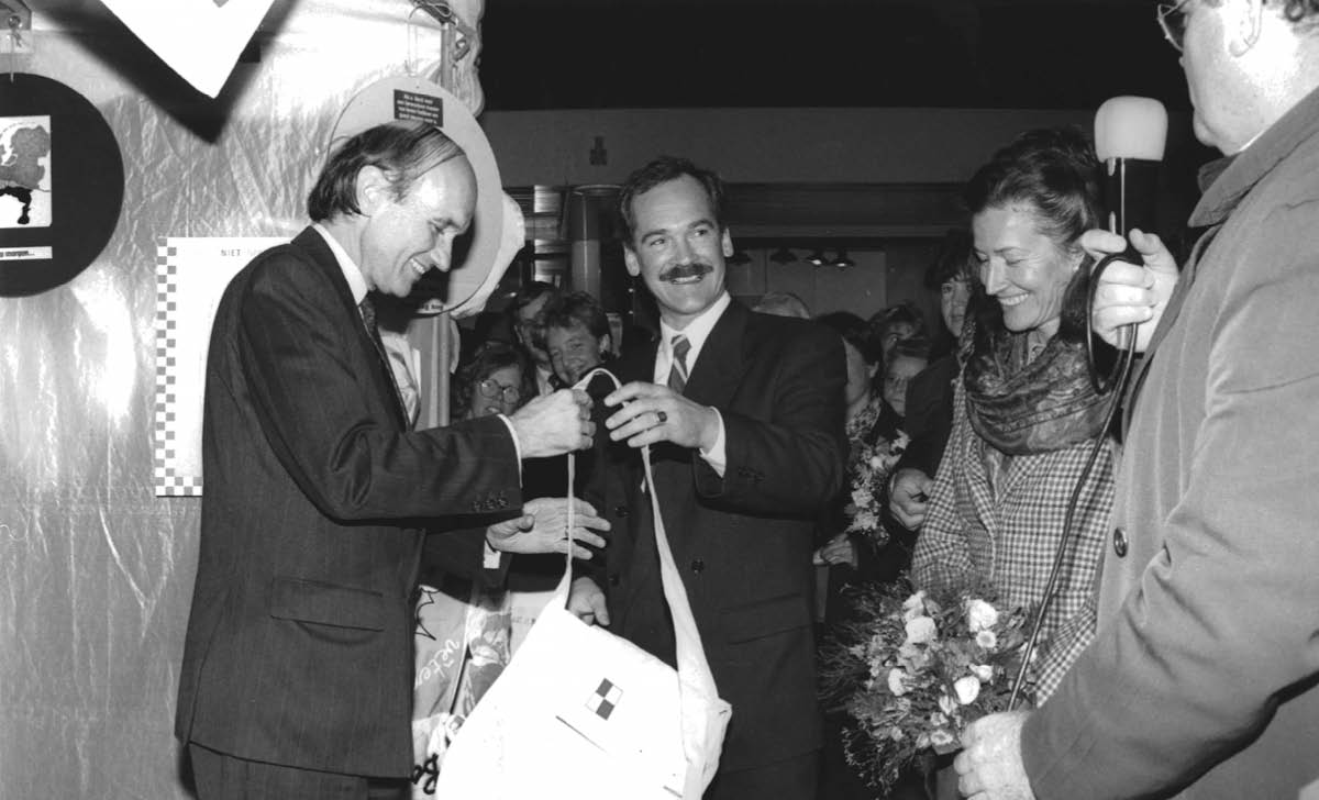 Zwart wit foto met 4 personen, waarbij de Commissaris van de Koningin een tas vastheeft. 