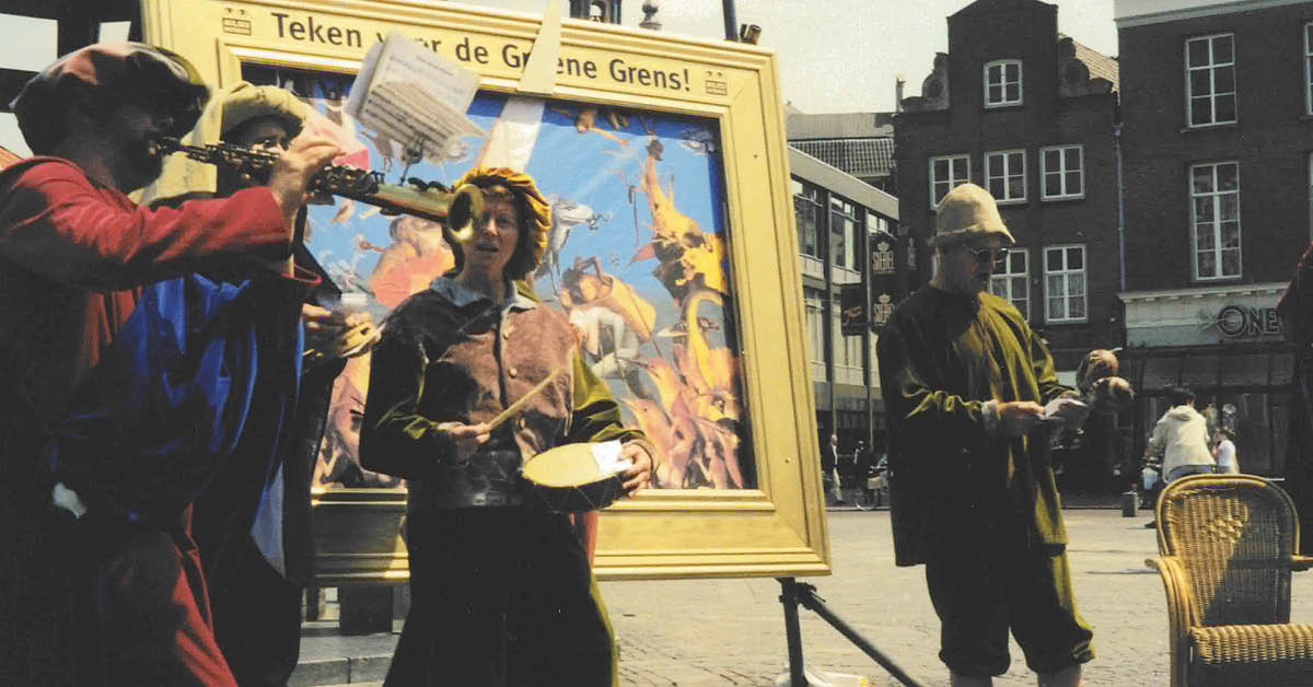 Personen verkleed in Jeroen Bosch-stijl, voor een schilderij van Jeroen Bosch met daarop de tekst 'Teken voor de Groene Grens'